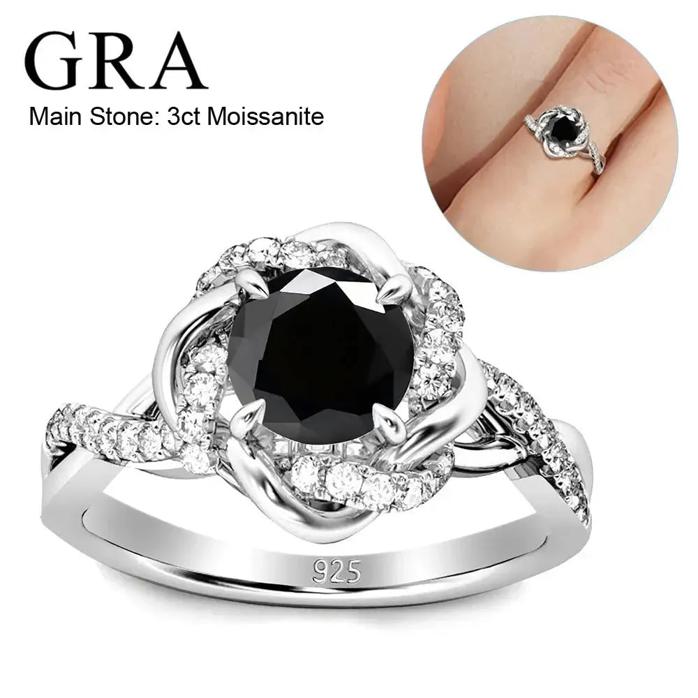 A silver ring featuring a 3-carat black moissanite as the main stone, surrounded by smaller clear stones in a twisted design. The band is engraved with "925," indicating sterling silver. An inset image shows the ring worn on a finger.